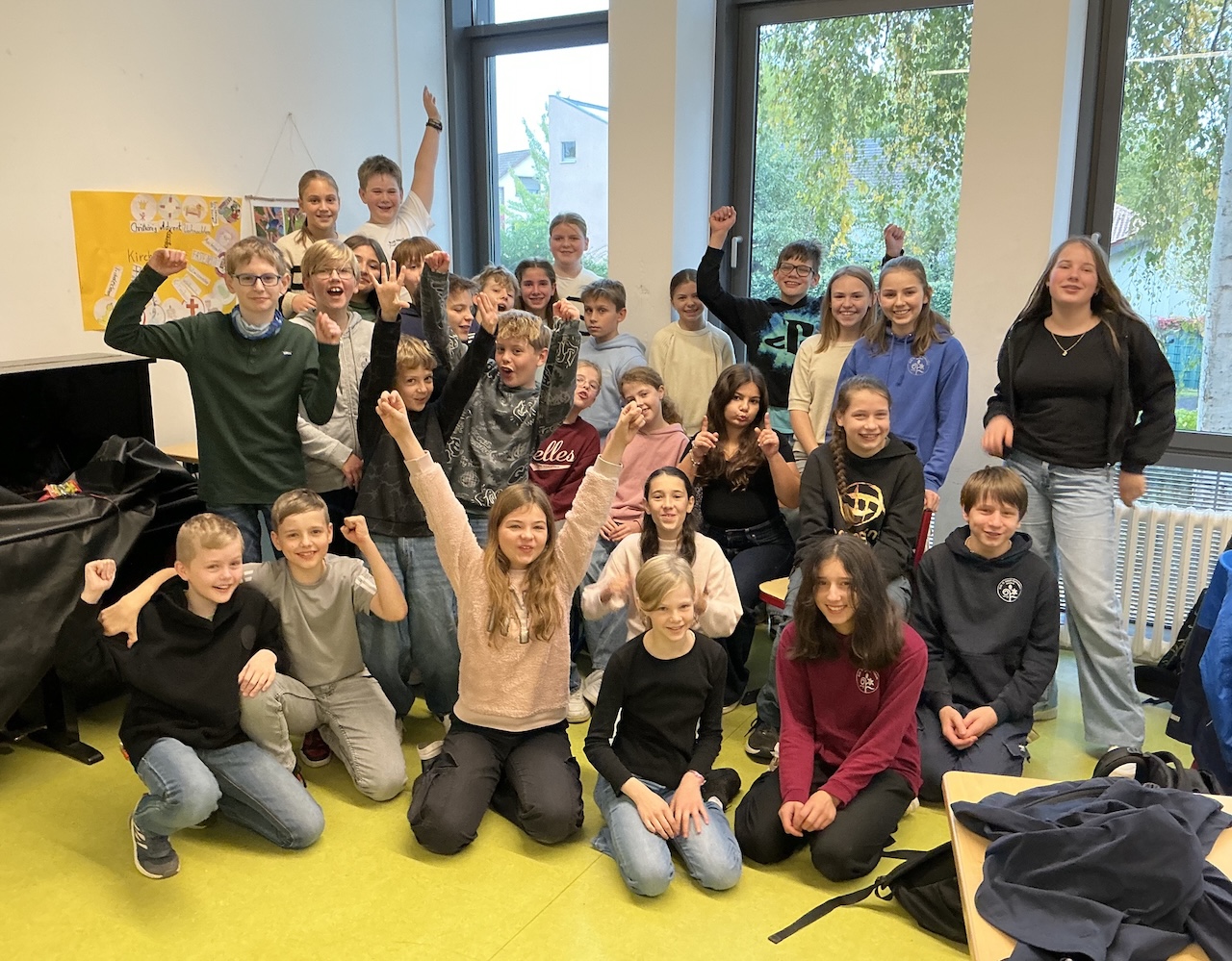 Gruppenfoto mit Schüler:innen, einige Arme sind jubelnd ausgestreckt