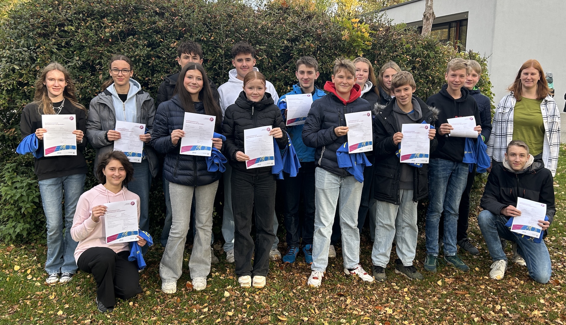Schülerinnen und Schüler, Urkunden und blaue Shirts in der Hand, Lehrerin am Rand