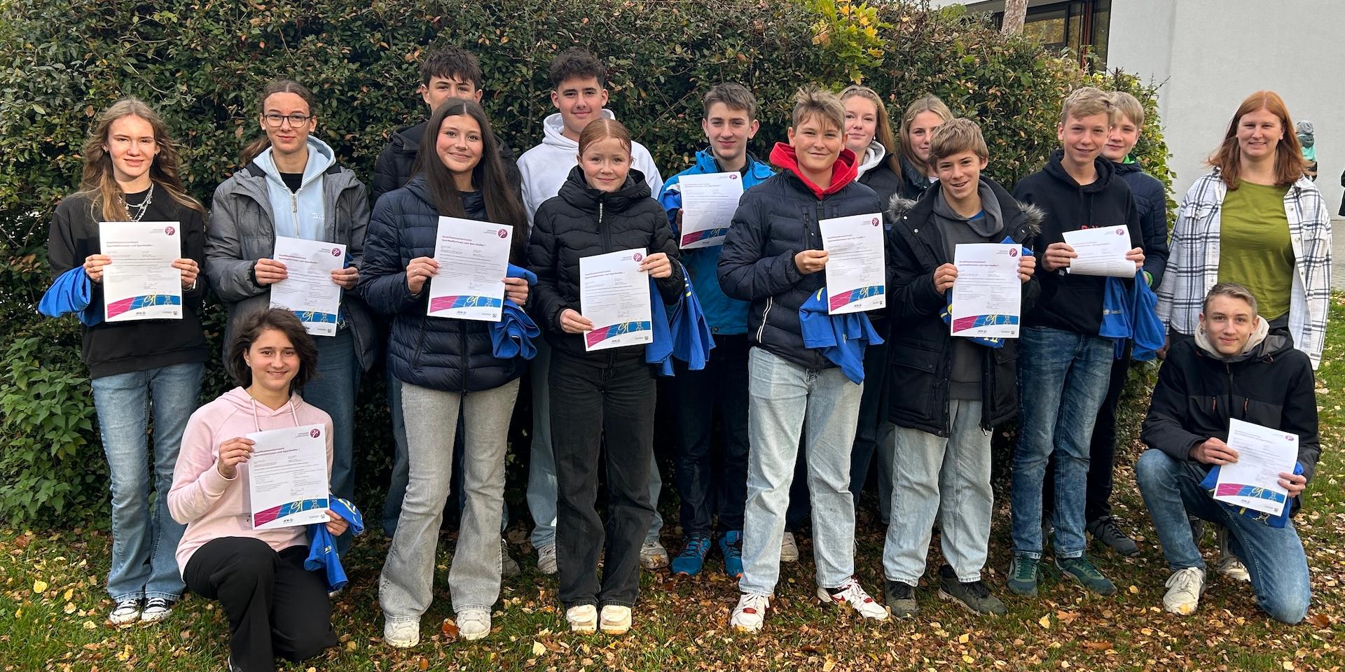 Schülerinnen und Schüler, Urkunden und blaue Shirts  in der Hand, Lehrerin am Rand