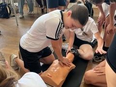 Schülerin übt an einer Puppe Herzdruckmassage, andere Schüler schauen zu