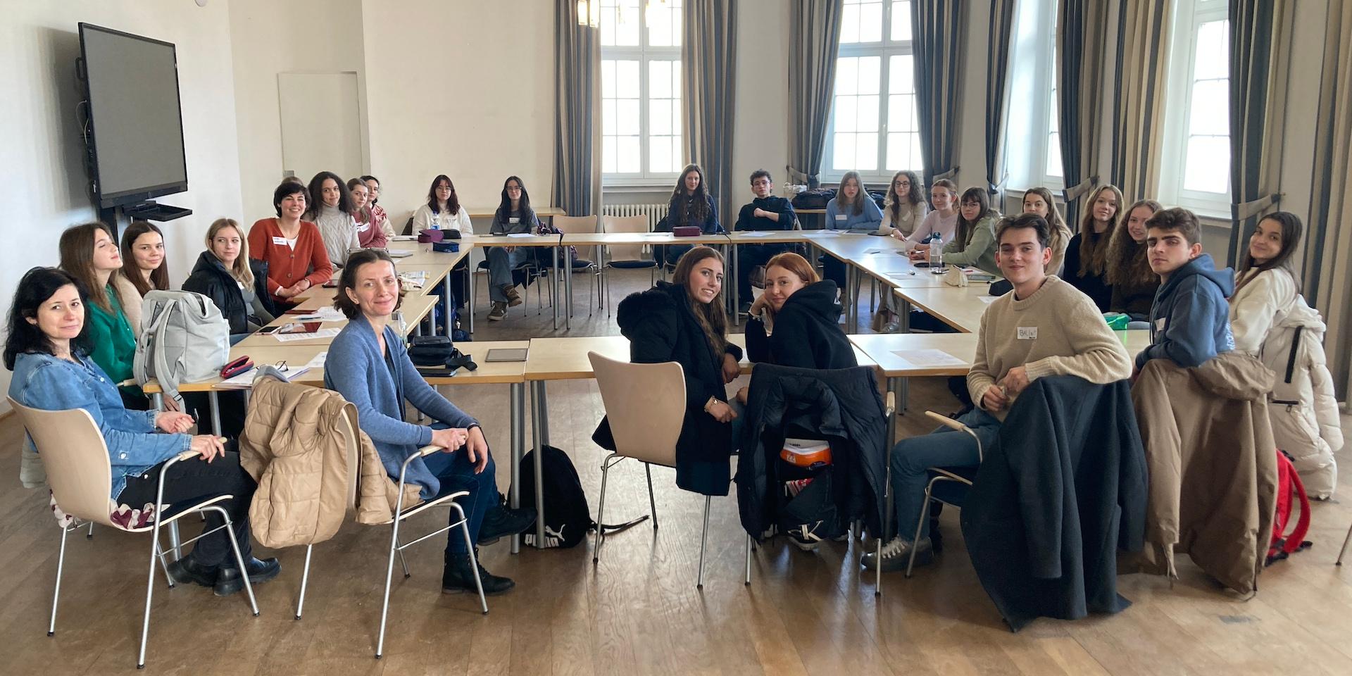 Ungarische und deutsche Schüler:innen sitzen an Tischen in einem Saal