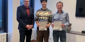 Drei Männer (Schulleiter, Schüler, Lehrer) stehen nebeneinander, Schüler und Lehrer halten Urkunden