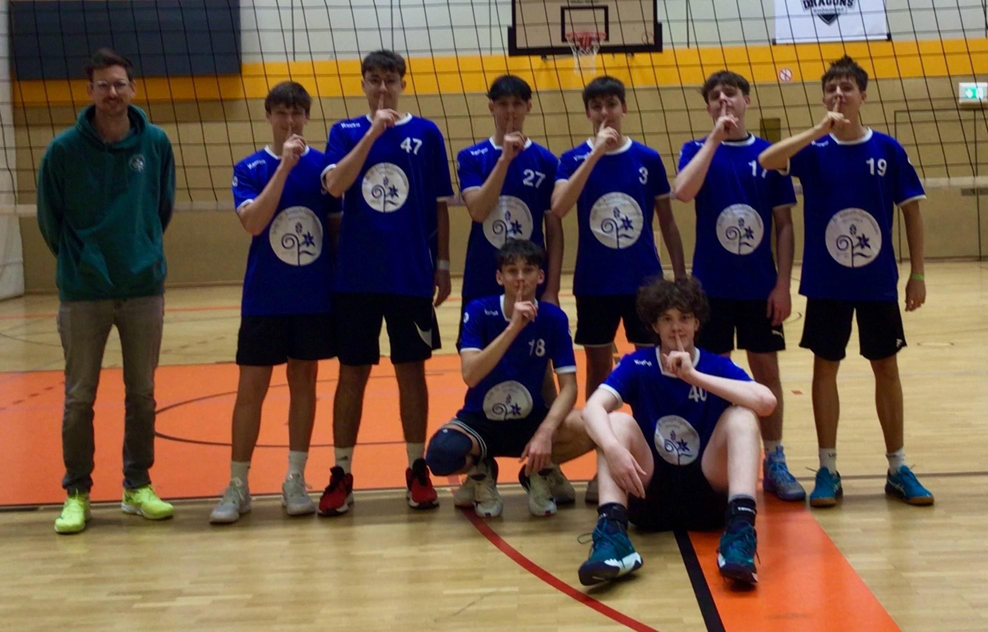 Mannschaftsfoto von Jungen in der Sporthalle vor Volleyballnetz mit Lehrer an der Seite