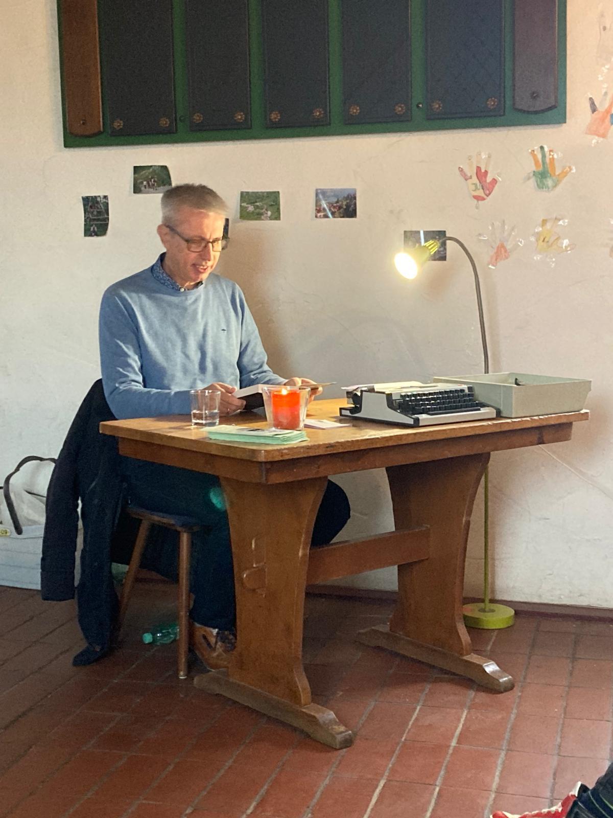 Mann am Tisch, liest vor, Kerze und Schreibmaschine auf dem Tisch