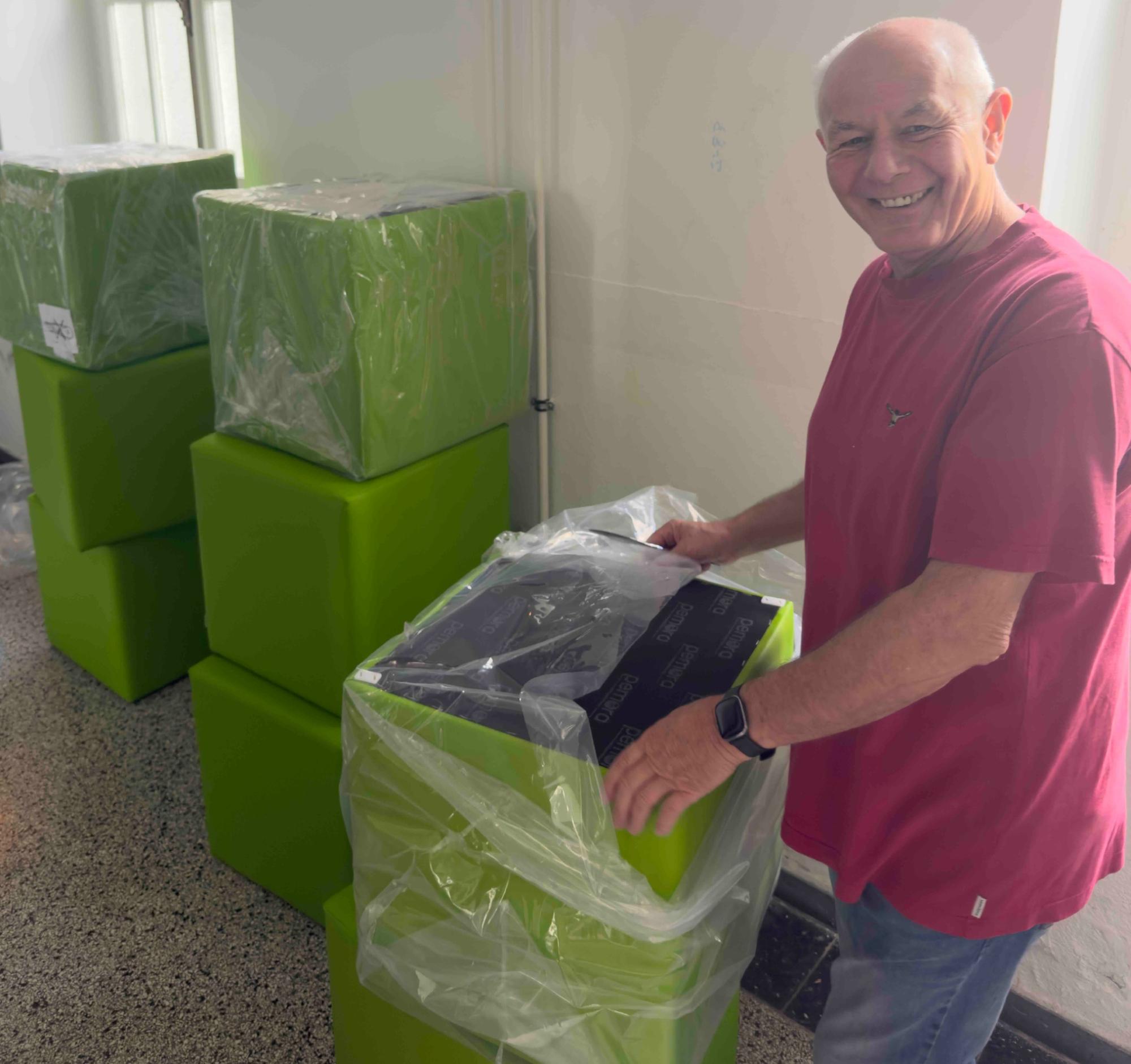 Hausmeister Andreas Gawenda packt die Sitzwürfel aus. 8 grüne Sitzwürfel in drei Stapen, z.T. in Folie, werden von einem Mann ausgepackt