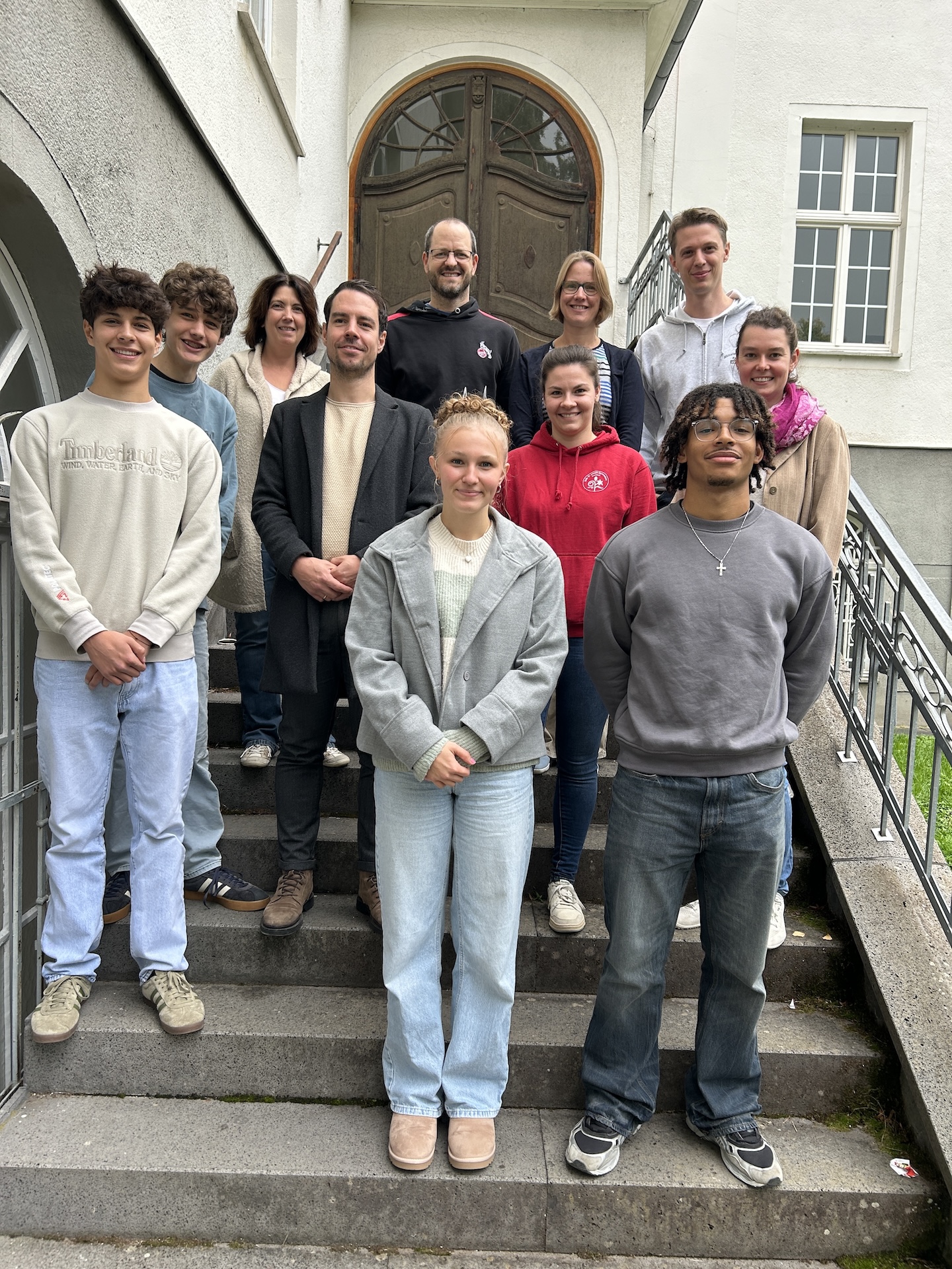 Gruppenfoto auf einer Treppe: Schülerin, drei Schüler, zwei Lehrerinnen, zwei Lehrer