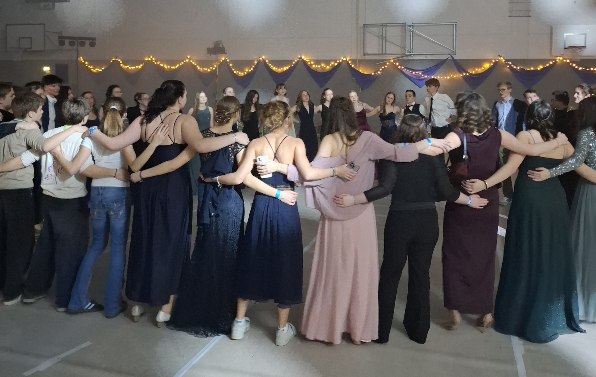 Schülerinnen und Schüler in Ballkleidern und Anzügen stehen umarmend im Kreis