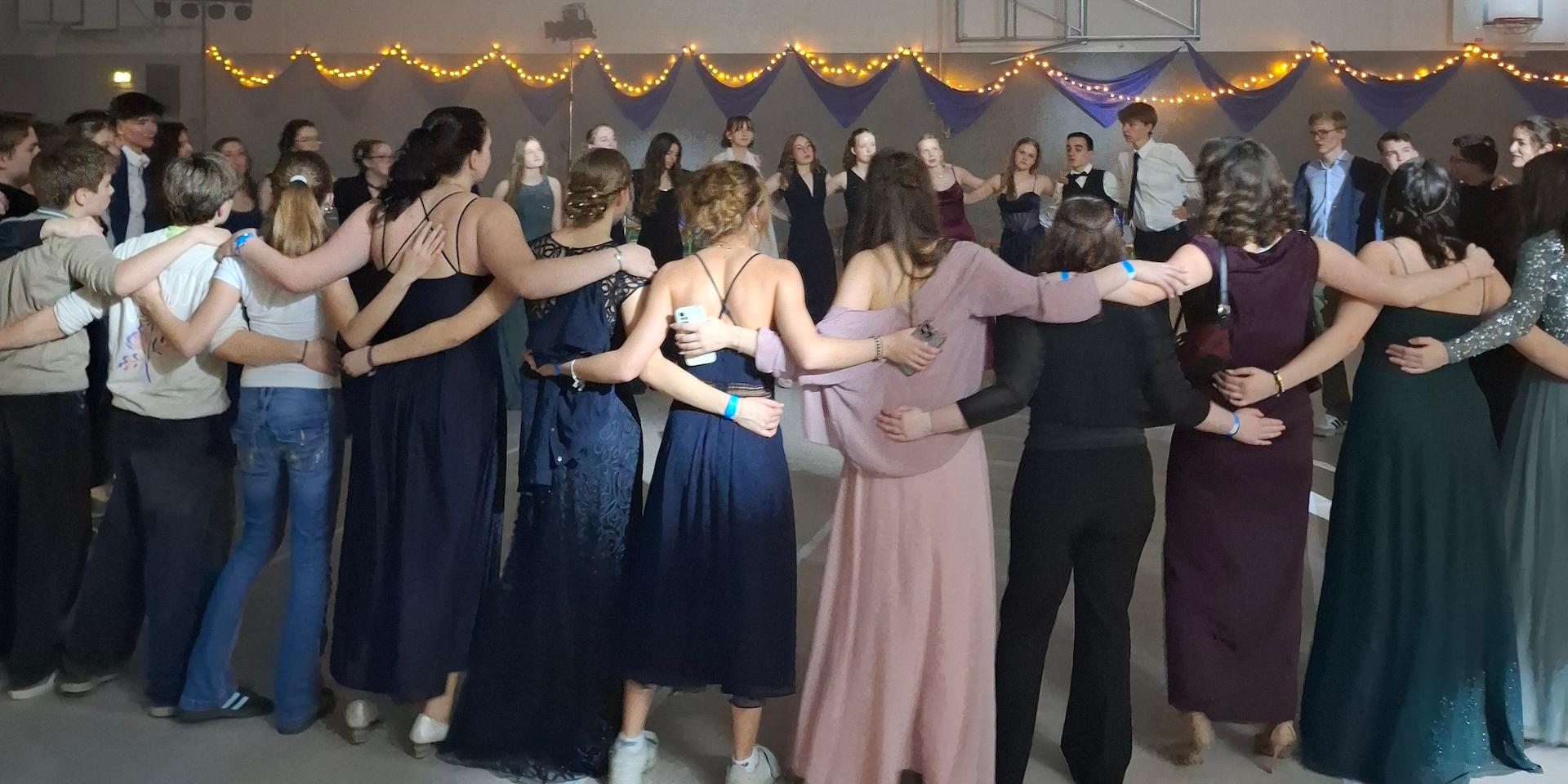 Schülerinnen und Schüler in Ballkleidern und Anzügen stehen umarmend im Kreis